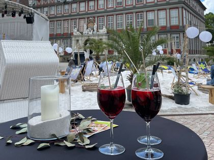Drinks in Weingläsern auf einem Tisch vor einem aufgeschütteten Strand vor dem Schloss