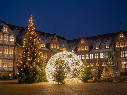 Ein Platz eingerahmt von Fachwerk wird stimmungsvoll von einer Tanne und einer übergroßen Weihnachtskugel beleuchtet